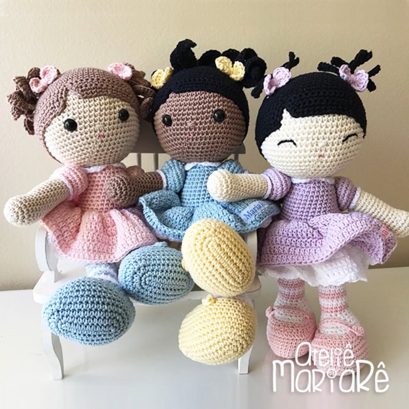 As três bonecas Melhores Amigas de crochê, Mari, Mirna e Miong, sentadas juntas em um banquinho branco