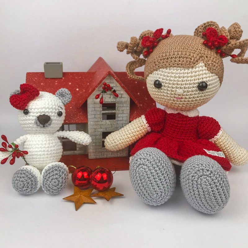 Boneca de crochê com vestido vermelho de Natal ao lado de um ursinho polar de amigurumi branco com laço vermelho, decoração natalina