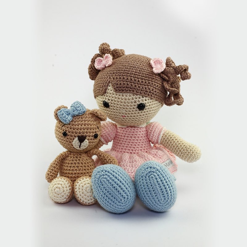 Boneca Mari de crochê ao lado de um ursinho de amigurumi com laço azul