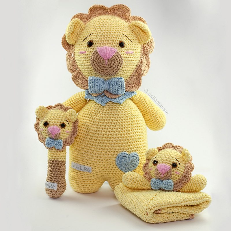 Família de leões de crochê amigurumi: um leão grande com gravata borboleta azul e dois filhotes pequenos, um deles em formato de chocalho