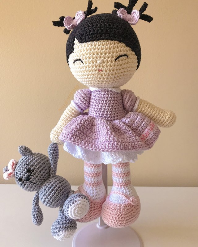 Boneca de crochê com vestido cinza e cabelo preto, em pé ao lado de um gatinho cinza de amigurumi