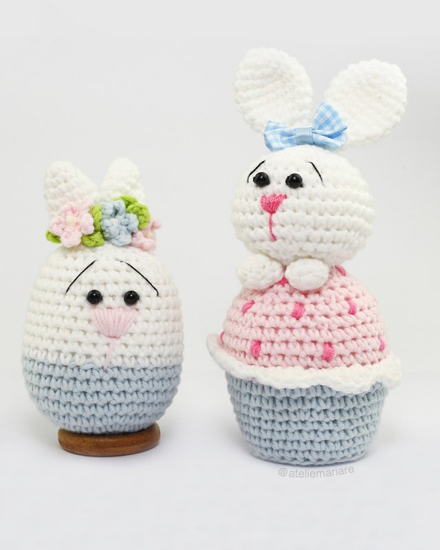 Duas coelhinhas de crochê amigurumi em formato de cupcake, uma com coroa de flores e outra com laço azul xadrez
