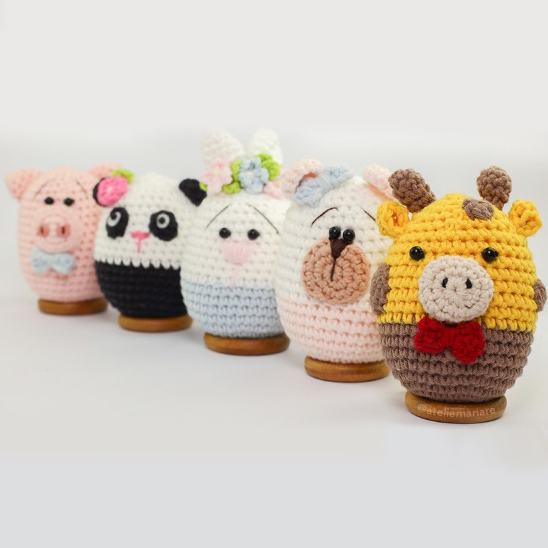 Cinco bichinhos de crochê amigurumi em formato de ovo: porquinho, panda, coelha, ursinho e girafa, em fileira