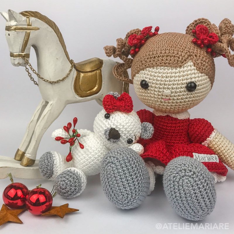 Boneca de crochê com vestido vermelho de Natal ao lado de um ursinho polar de amigurumi e um cavalinho de balanço decorativo