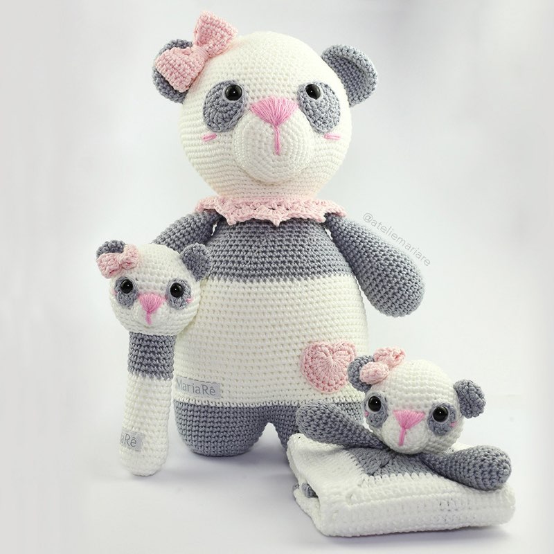 Família de pandas de crochê amigurumi com laço rosa: um panda grande e dois filhotes pequenos, um deles em formato de chocalho