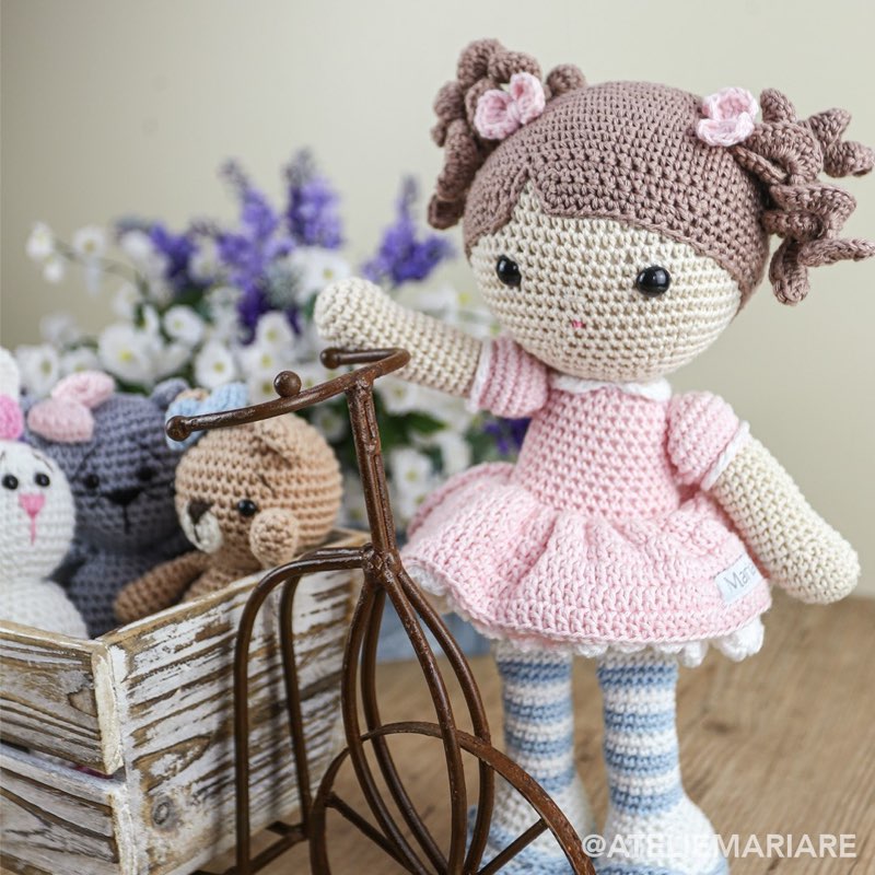 Boneca de crochê com vestido rosa ao lado de uma gatinha, sobre uma cesta de bicicleta com flores de lavanda