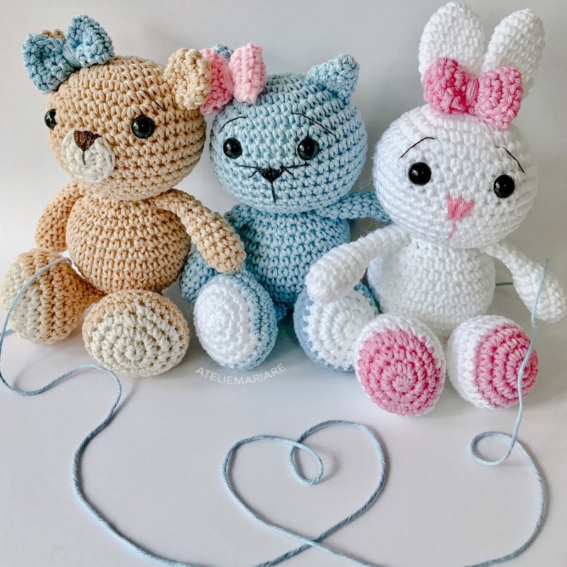 Trio de bichinhos de crochê amigurumi (urso, gatinho e coelha) formando um coração com um fio
