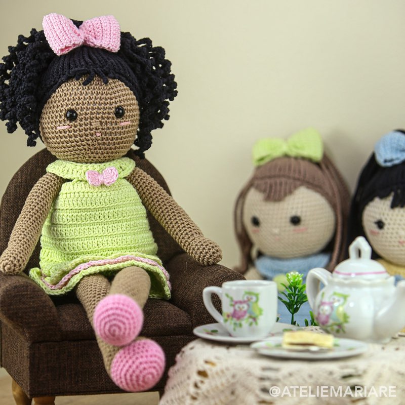 Boneca de crochê tomando chá ao lado de uma corujinha de amigurumi, com bule e xícaras em miniatura