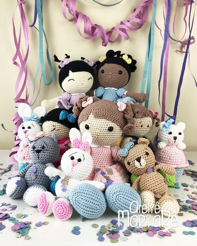 Grande grupo de bonecas e bichinhos de crochê amigurumi reunidos entre flores e fitas coloridas