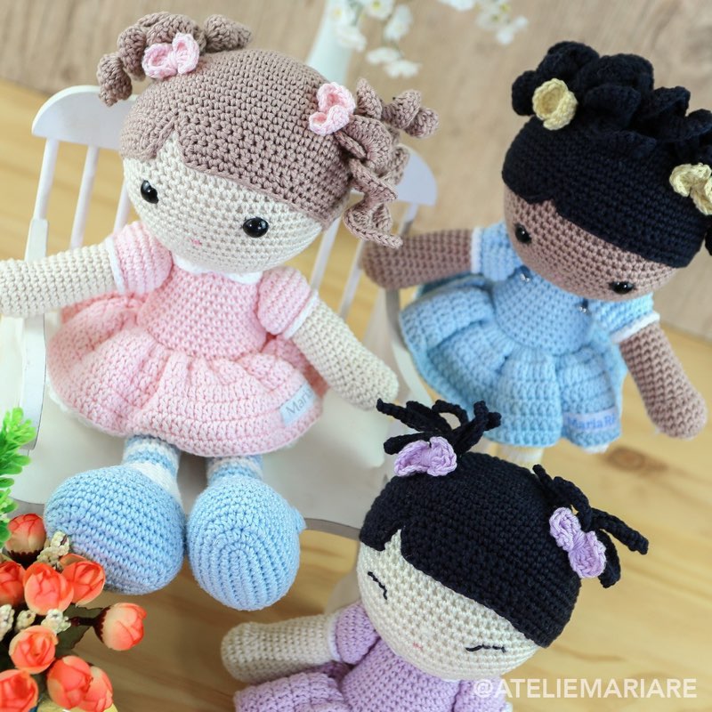 Duas bonecas de crochê com vestidos rosa e cabelo escuro, sentadas lado a lado