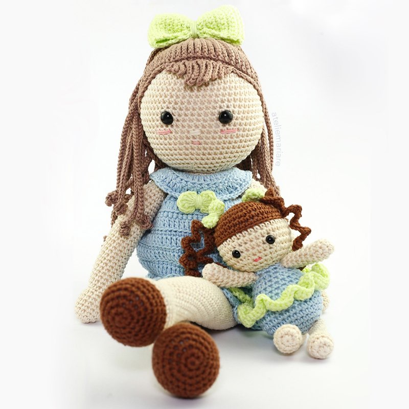 Boneca de crochê com vestido azul sentada ao lado de uma bonequinha bebê com roupinha verde