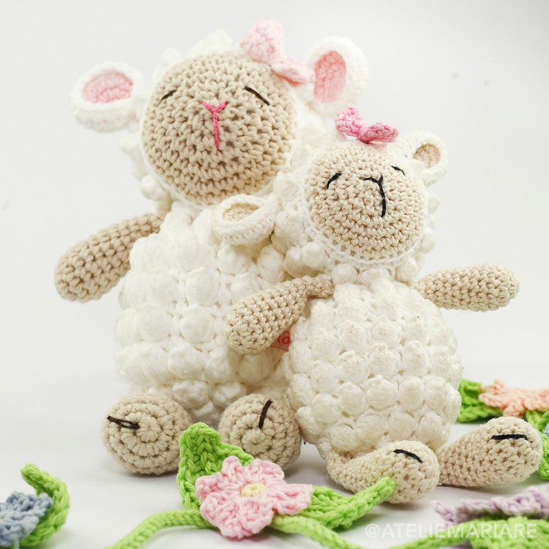 Família de ovelhinhas de crochê amigurumi, uma grande e duas pequenas, com laço rosa e flores